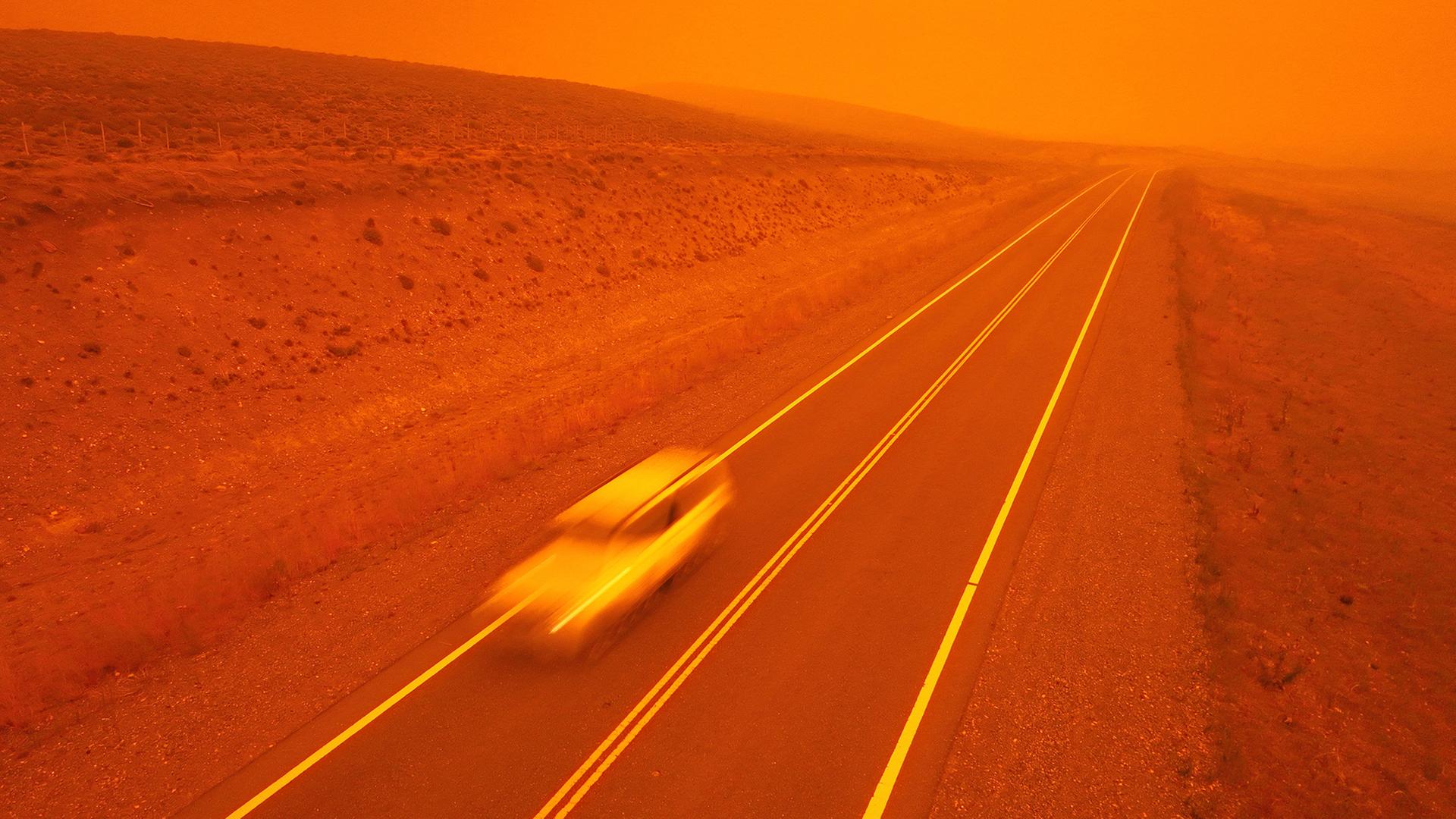 Ein Auto rast Ã¼ber eine StraÃe, wÃ¤hrend der Rauch von WaldbrÃ¤nden den Himmel in der NÃ¤he von Cholila (Argentinien) rot fÃ¤rbt. | AP