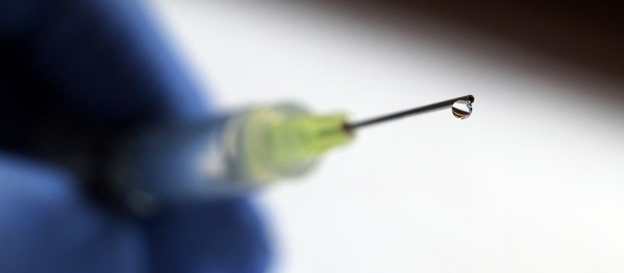 Eine Flüssigkeit tropft aus der Kanüle einer Spritze.