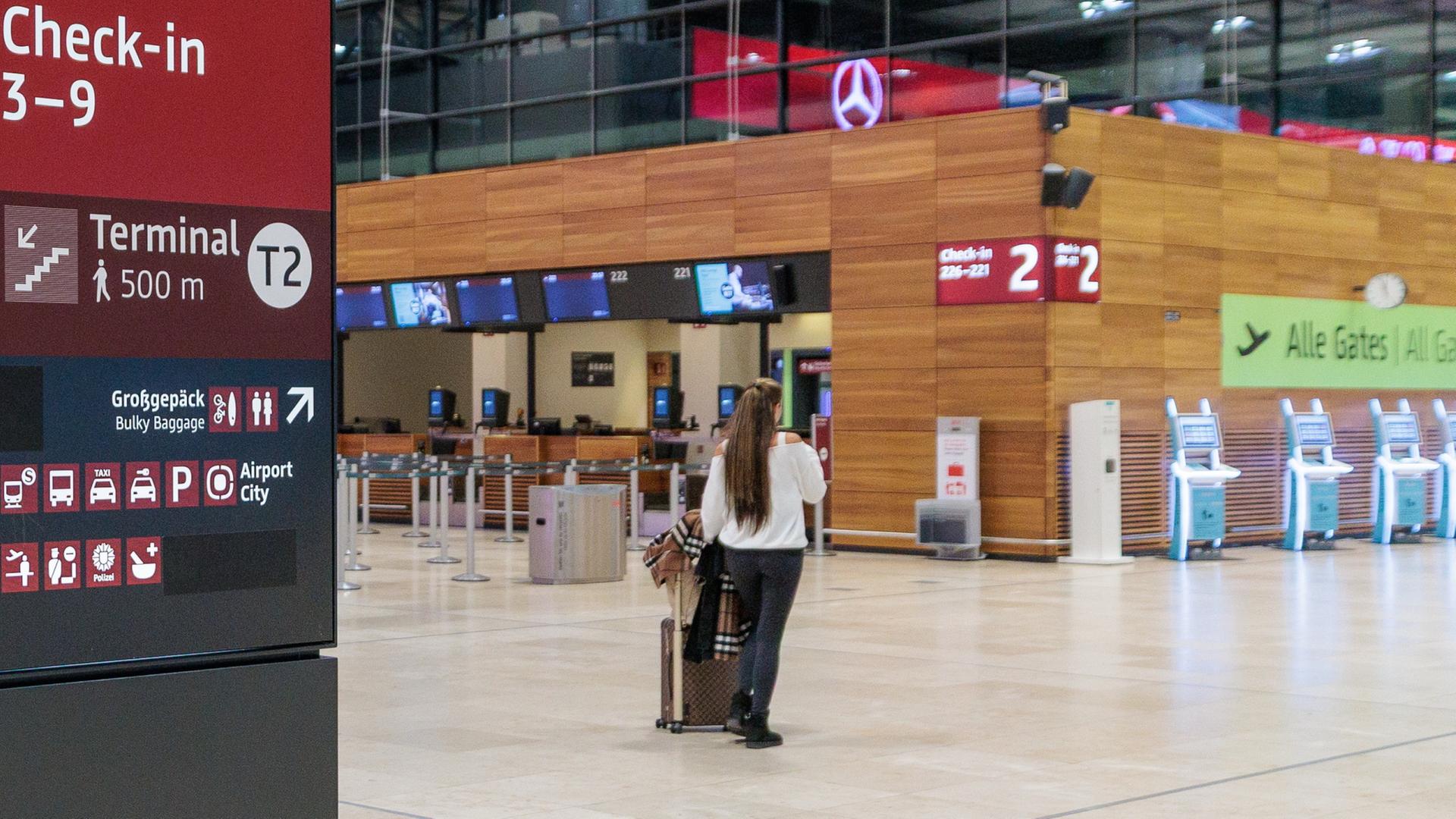 Eine Frau mit Rollkoffer steht in einer Halle am Flughafen BER  | dpa