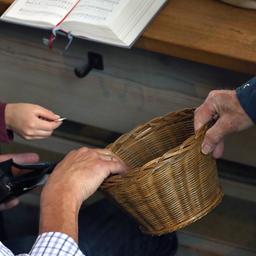 Besucher eines katholischen Gottesdienstes spenden Geld in einen herumgereichten Korb.