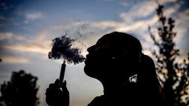 Eine junge Frau raucht mit einer E-Shisha und ist dabei als Silhouette zu sehen.