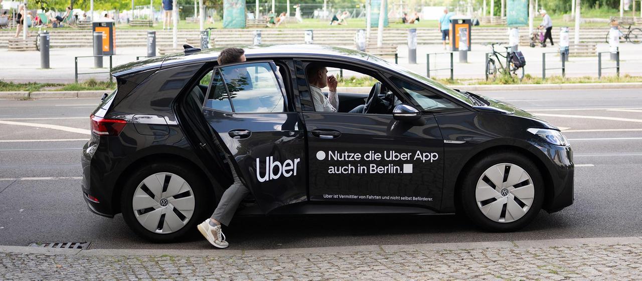 Ein Mann steigt in einen Mietwagen mit dem Schriftzug des Mobilitätsdienstleisters und Fahrtenvermittlers Uber ein.