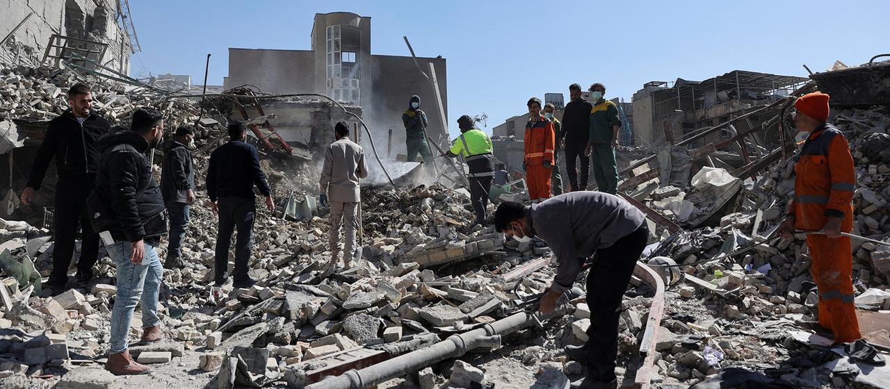 Menschen stehen vor Trümmern vor einer Polizeistation in Teheran.
