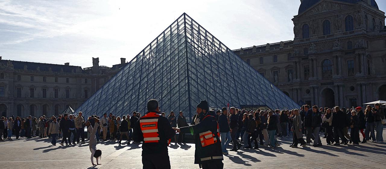 Sicherheitspersonal steht in der Nähe der Glaspyramide, während Menschen Schlange stehen, um das Louvre-Museum zu betreten. 