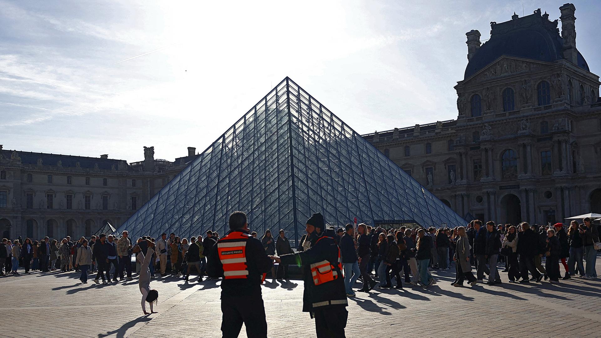 Sicherheitspersonal steht in der Nähe der Glaspyramide, während Menschen Schlange stehen, um das Louvre-Museum zu betreten.  | REUTERS