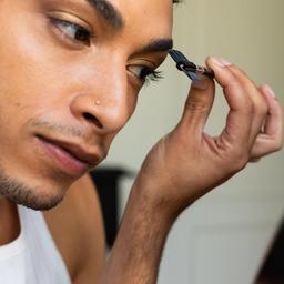 Ein transgender Mann schminkt sich und blickt in den Spiegel.