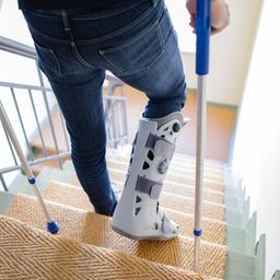 Ein Mann geht mit Krücken und einer Orthese eine Treppe hinunter. 