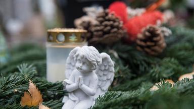 Eine Engelsfigur und ein Blumengesteck mit Kerze auf einem Grab.