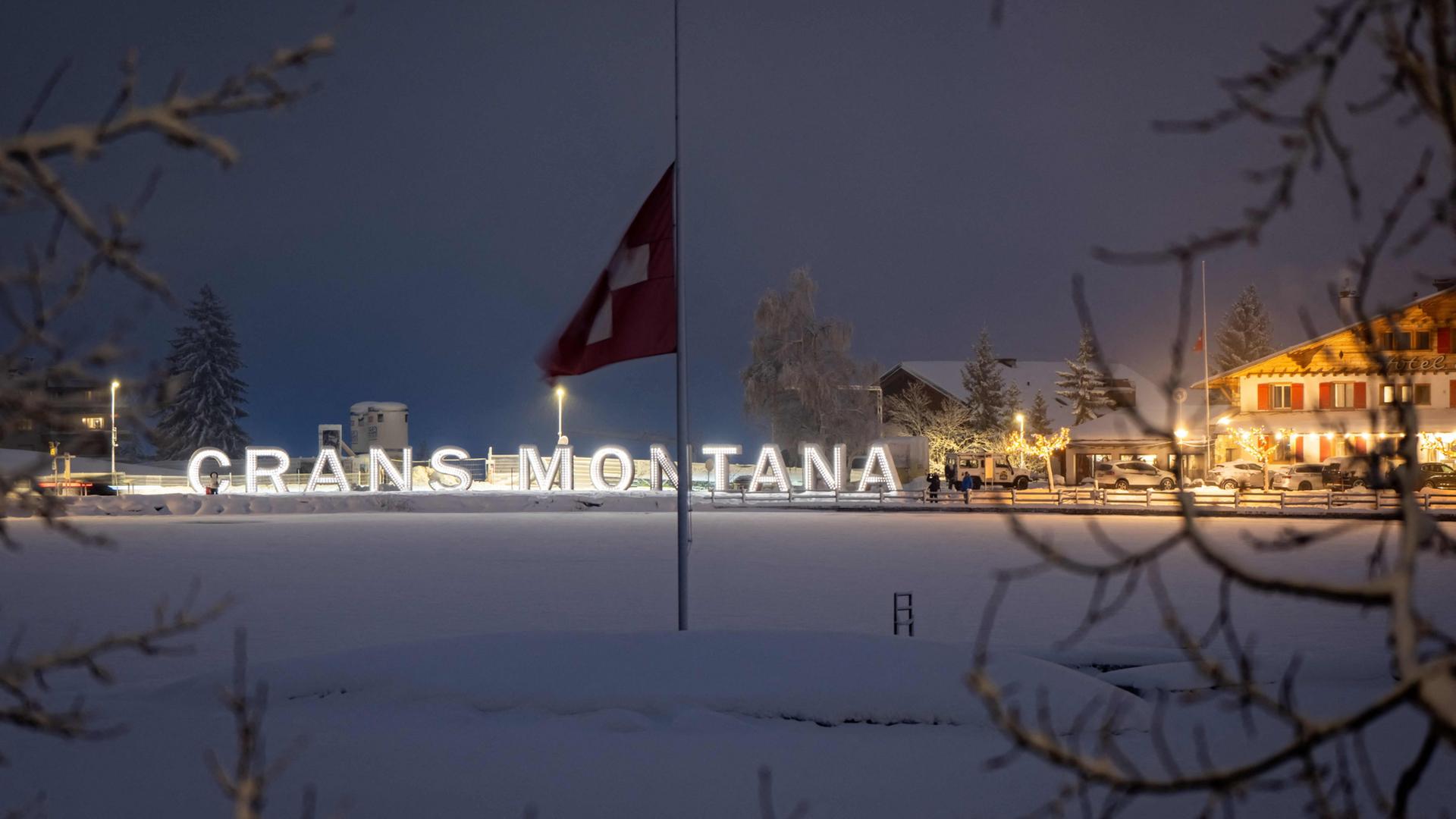 Die Schweizer Flagge weht vor einer Leuchtschrift in Crans-Montana. | AFP