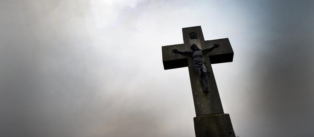 Ein Kreuz ist vor einem wolkenverhangenen Himmel zu sehen.
