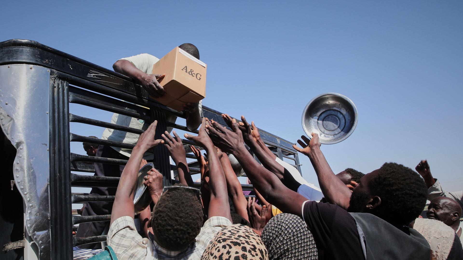 Sudanesische Familien strecken die Hände nach Hilfsgütern aus, die im Lager El-Afadh in Al Dabbah im Nordstaat des Sudans verteilt werden | AP Photo/Marwan Ali