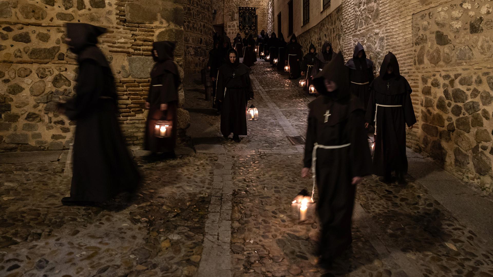 Menschen in schwarzen Roben mit weiÃen Kordeln tragen Laternen durch eine gepflasterte Gasse in Toledo. | EPA