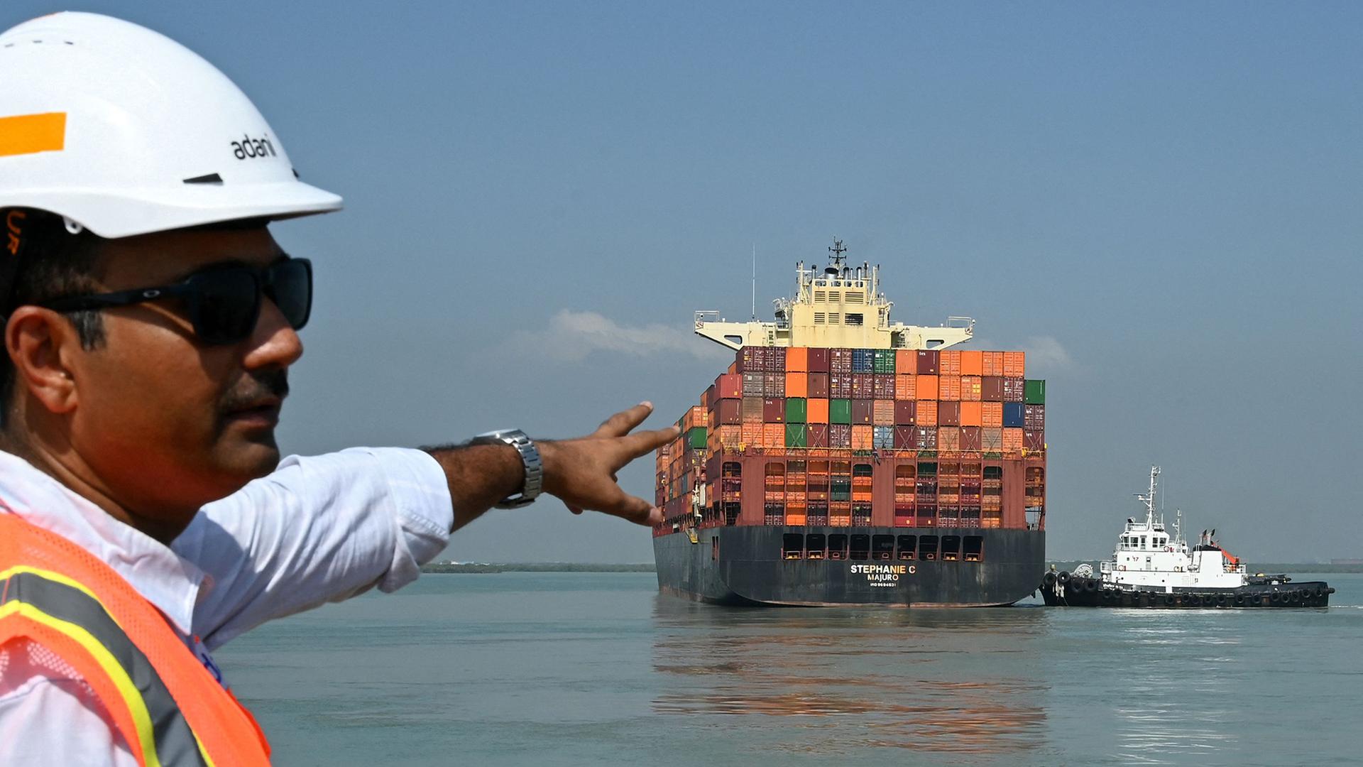 Ein Mitarbeiter zeigt auf ein Containerschiff, das den Hafen Mundra in Mundra (Indien) verlässt. | AFP