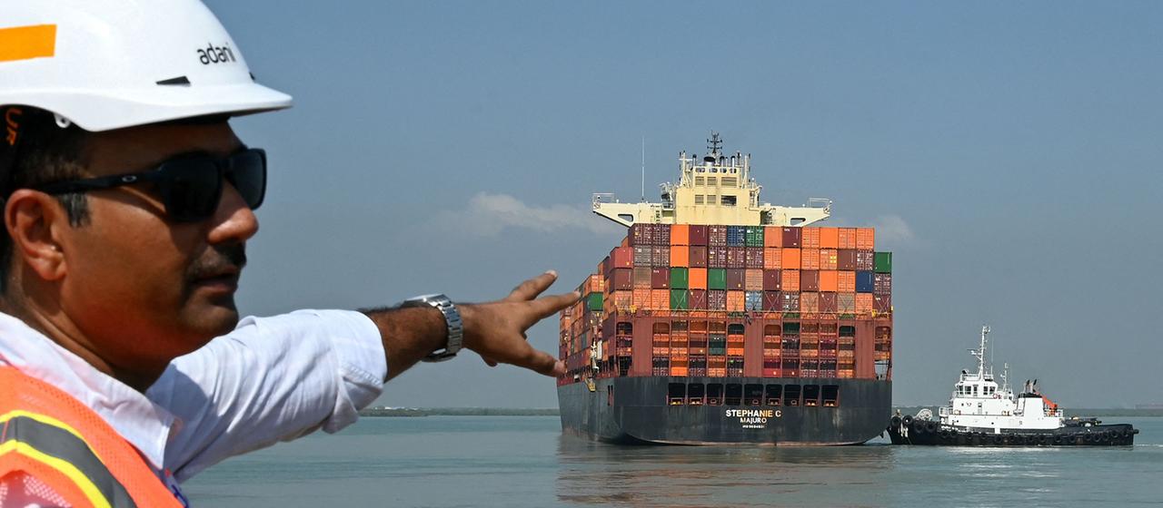 Ein Mitarbeiter zeigt auf ein Containerschiff, das den Hafen Mundra in Mundra (Indien) verlässt.