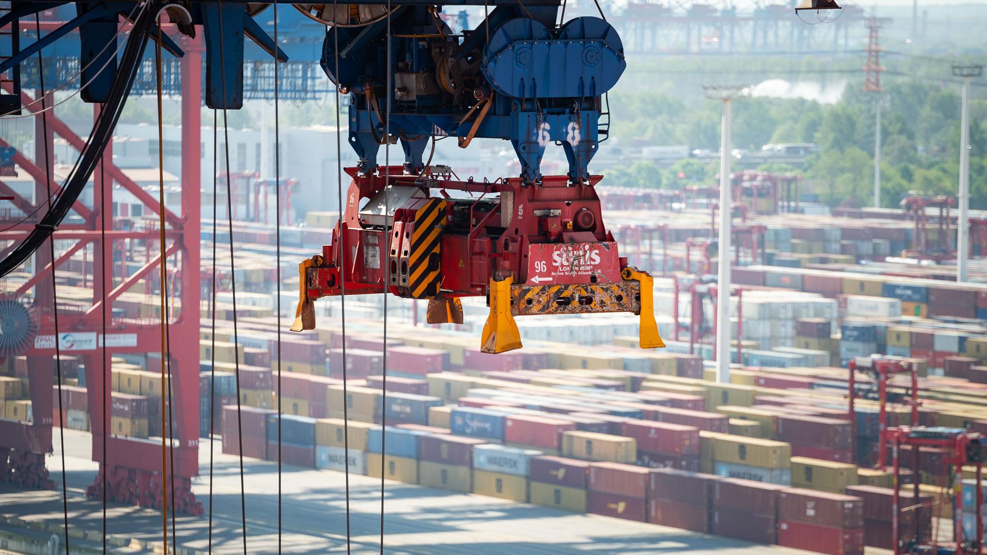 Ein leerer Greifer einer Containerbrücke schwebt über einem Schiff.  | picture alliance/dpa