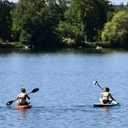 Stand-up-Paddler sind bei sommerlichen Temperaturen auf dem Badesee in Trais-Horloff unterwegs.