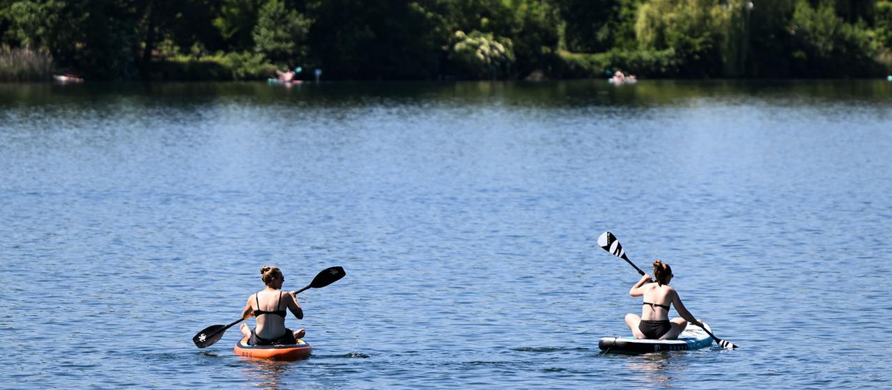 Stand-up-Paddler sind bei sommerlichen Temperaturen auf dem Badesee in Trais-Horloff unterwegs.
