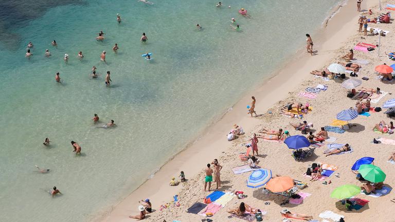 Menschen schwimmen und sonnen sich am Strand von Portals Nous auf Mallorca. 