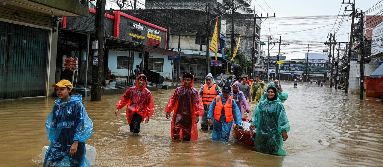 Freiwillige mit Hilfsgütern waten durch ein überschwemmtes Gebiet in der Provinz Songkhla (Thailand).