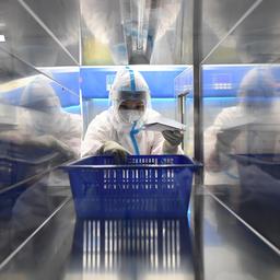 Eine medizinische Angestellte trägt einen Schutzanzug und hat einen blauen Korb in der Hand, während sie in einem chinesischen Testlabor für Corona-Tests arbeitet.