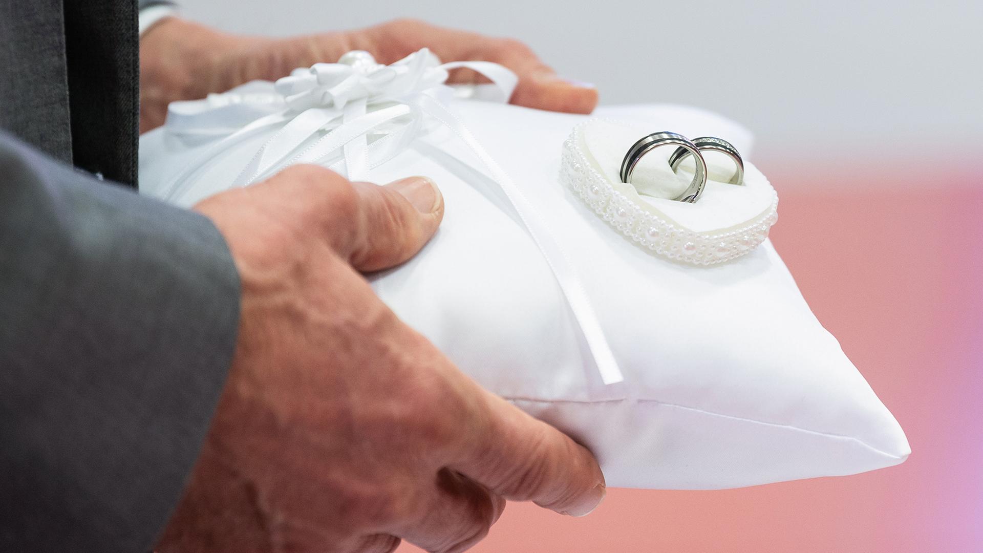 Ein Mann trägt ein Kissen mit zwei Eheringen. | dpa