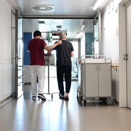 Ein Pfleger geht mit einem Patienten über einen Krankenhausflur. 