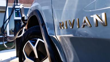 Rivian-Logo auf einem Elektroauto an einer Ladesäule.