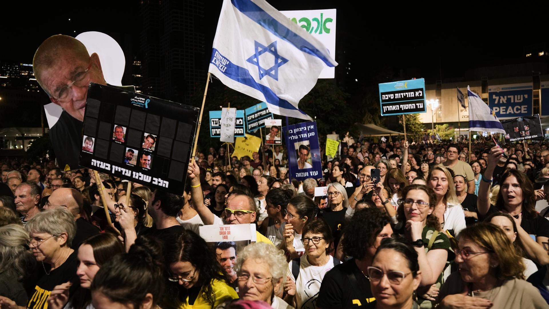 Menschen mit einer Israel-Fahne und Bannern protestieren in der Dunkelheit. | dpa