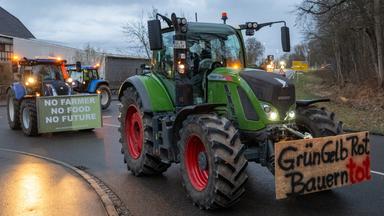 Nach einer Kundgebung des Bauernverbandes gegen die Sparpläne der Bundesregierung fahren Landwirte im Konvoi durch die Stadt Günzburg, auf einem Plakat steht "GrünGelbRot Bauern tot". 