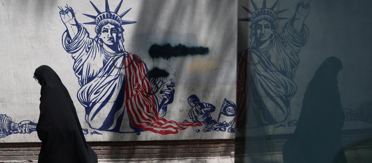 Eine verschleierte Frau läuft an einer Wand mit einem Anti-US-Graffiti vorbei