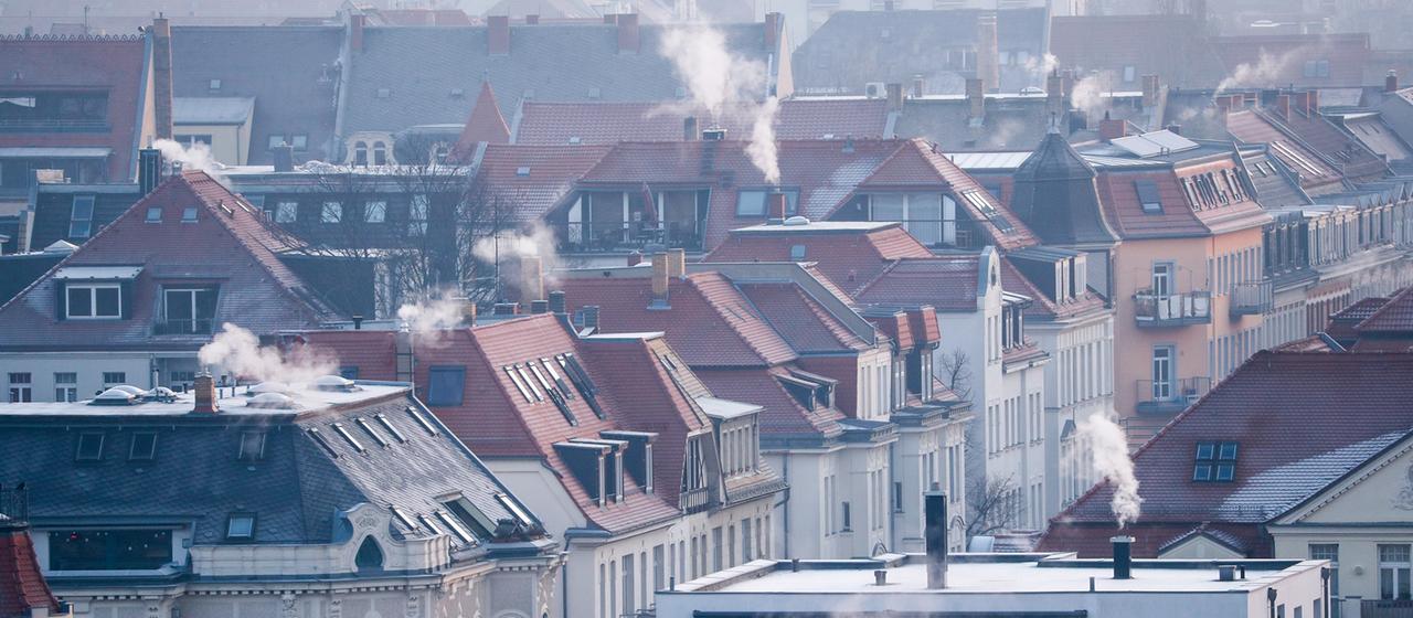 Rauch strömt aus den Kaminen auf den Dächern der Mehrfamilienhäuser im Leipziger Süden an einem kalten Wintermorgen.