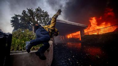 Ein Feuerwehrmann springt über eine Mauer, während Löscharbeiten im Stadtteil Pacific Palisades bekämpft.