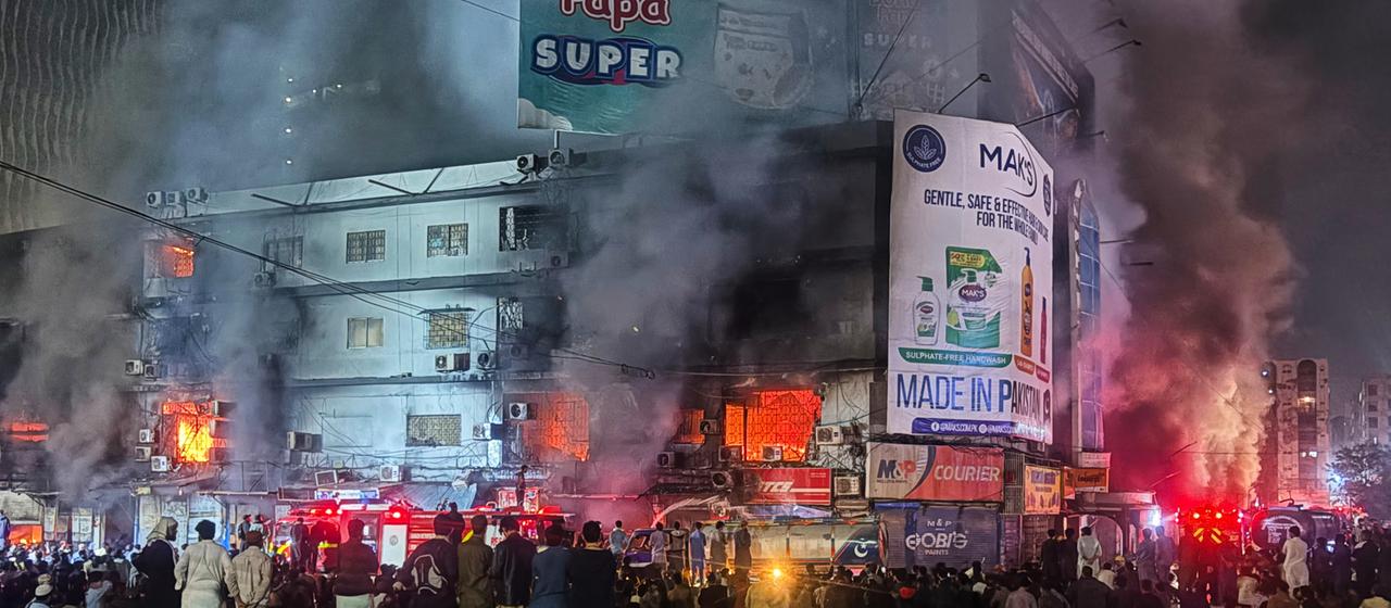 Viele Menschen stehen vor einem brennenden Einkaufszentrum in Karachi, Pakistan.
