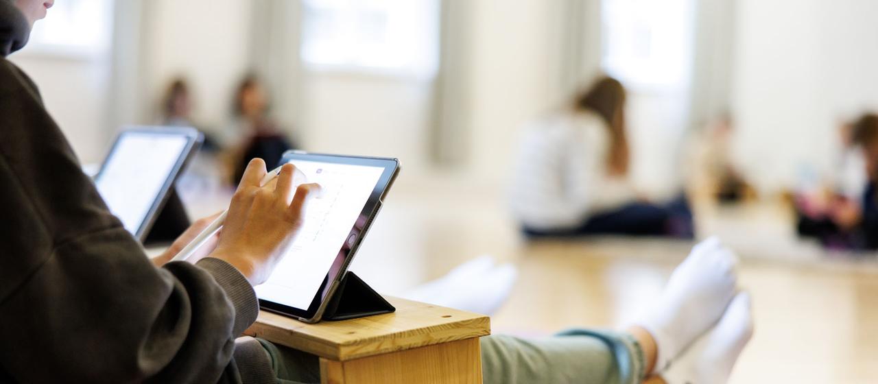 Eine Schülerin sitzt auf dem Boden und bedient ein Tablet.