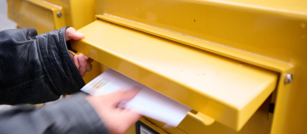 Eine Person wirft einen frankierten Brief in einen Briefkasten. 