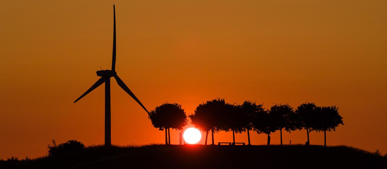 Die Sonne geht am Kronsberg hinter einem Windrad auf.