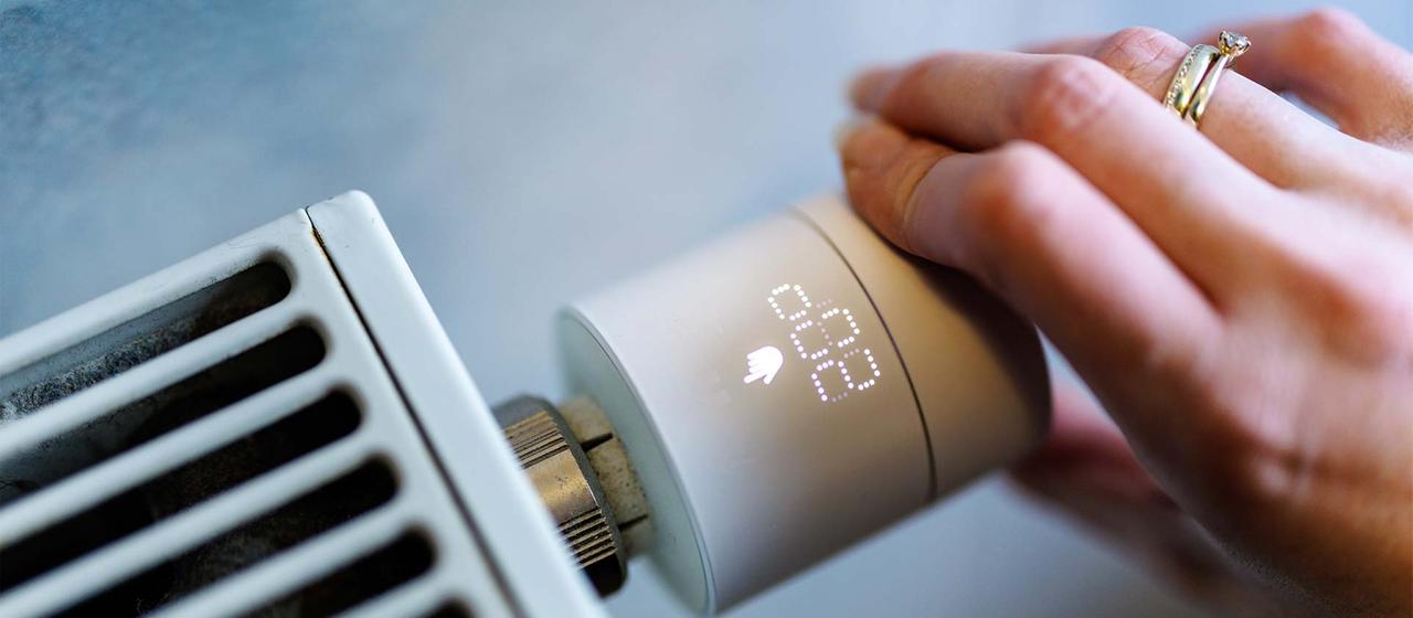 Eine Hand stellt an einem smarten Thermostaten die Temperatur ein.