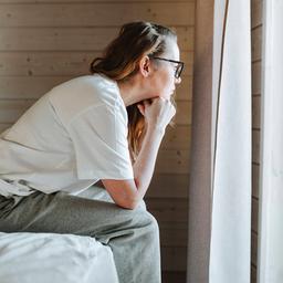 Eine Frau sitzt auf einem Bett und guckt aus dem Fenster.