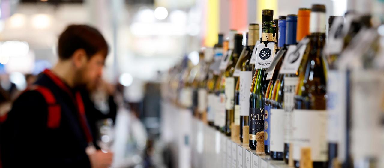 Besucher auf einer Weinmesse stehen vor einer Reihe von Weinflaschen.