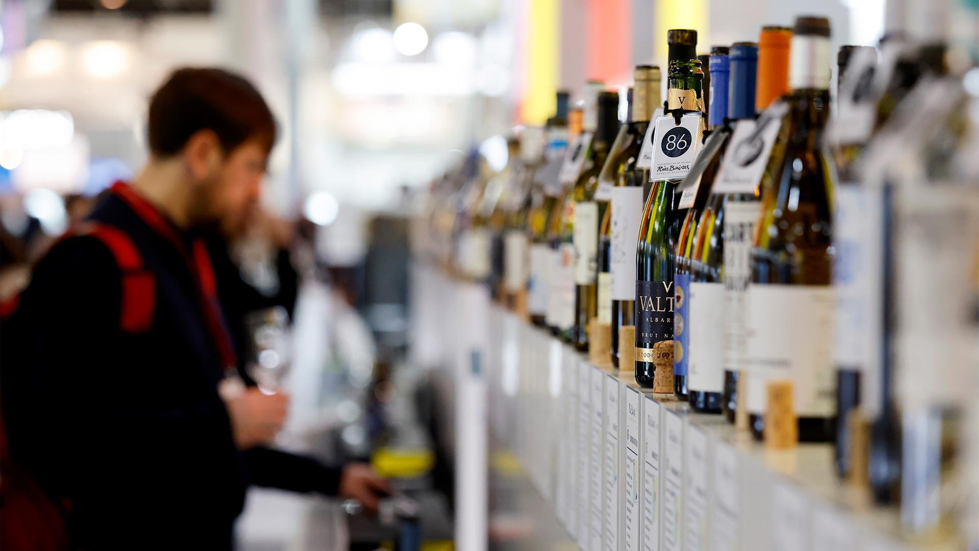 Besucher auf einer Weinmesse stehen vor einer Reihe von Weinflaschen. | picture alliance / Panama Pictur