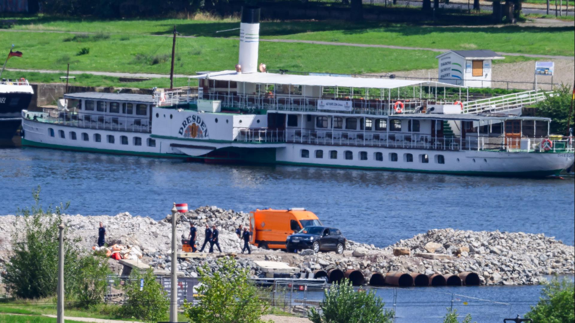 An einem Fluss stehen zwei Autos und Menschen die eine Bombe entschärfen | dpa