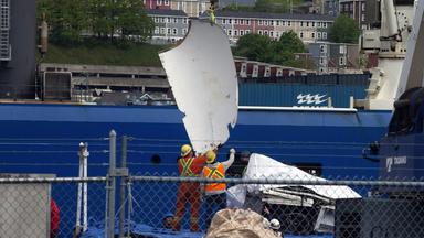 Zwei Männer mit Sicherheitswesten und Schutzhelmen bergen ein Trümmerteil de Tauchboots "Titan", das im kanadischen St. John's mit einem Kran von Bord der "Horizon" Arctic" gehoben wird.