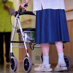 Eine ältere Dame geht mit ihrem Rollator über einen Flur in einer Pflegeeinrichtung.