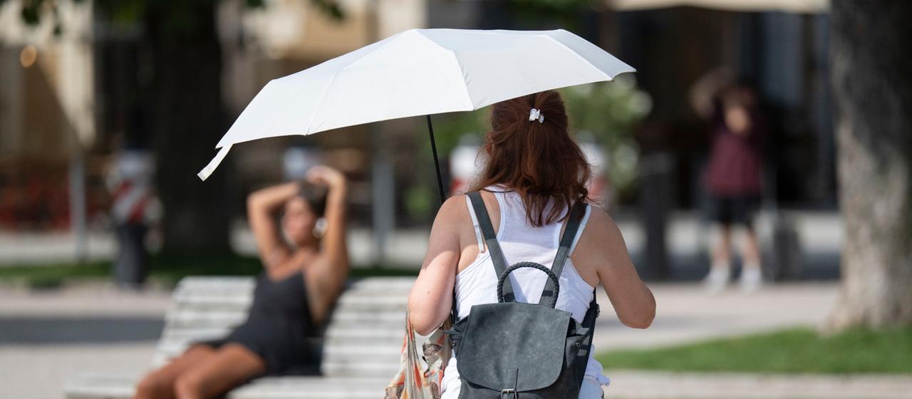 Eine Frau schützt sich mit einem Schirm vor der Sonne