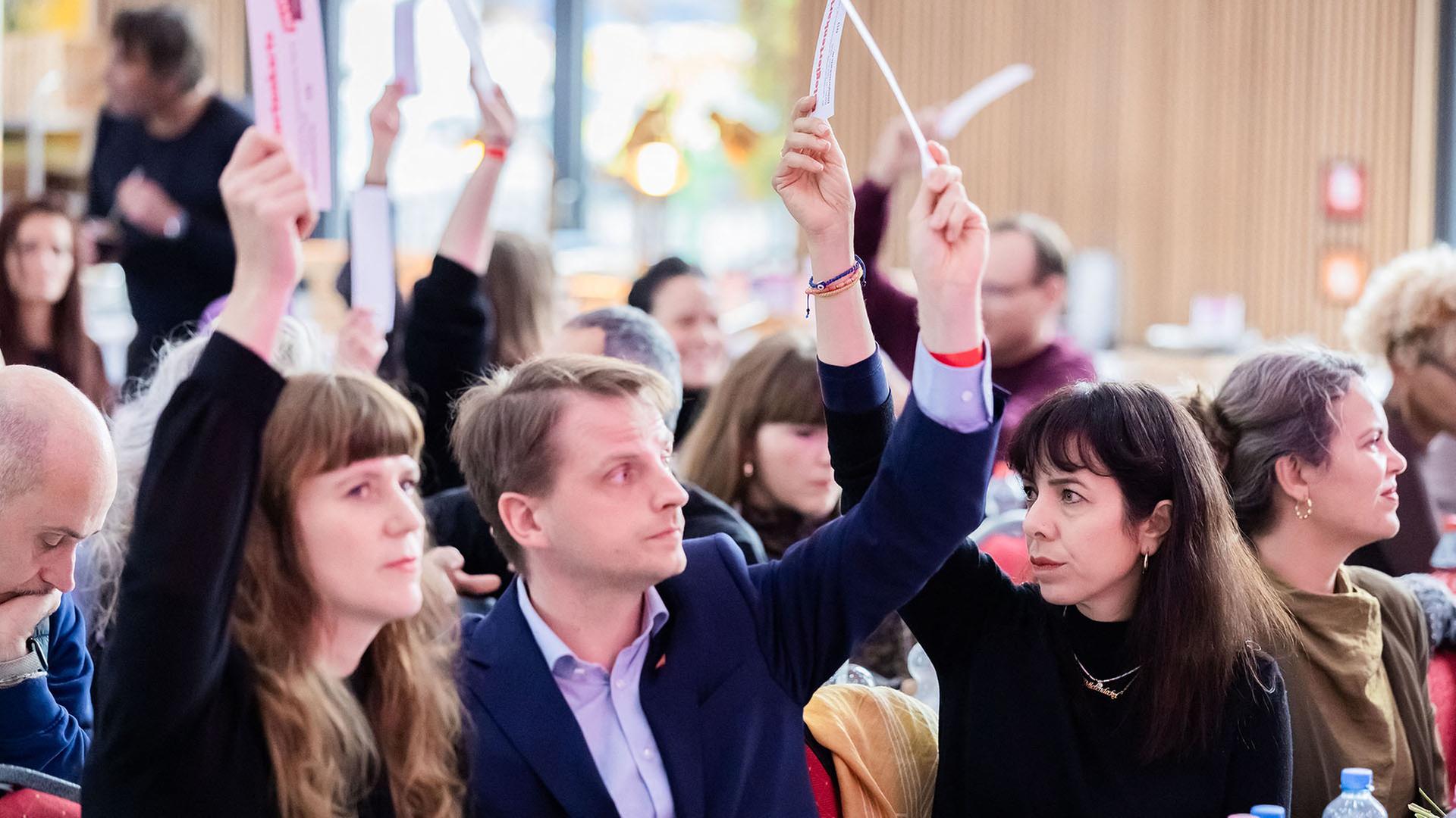 Kerstin Wolter, Maximilian Schirmer und Elif Eralp sitzen nebeneinander in einem Saal und heben Abstimmungskarten in die Luft. | Christoph Soeder/dpa