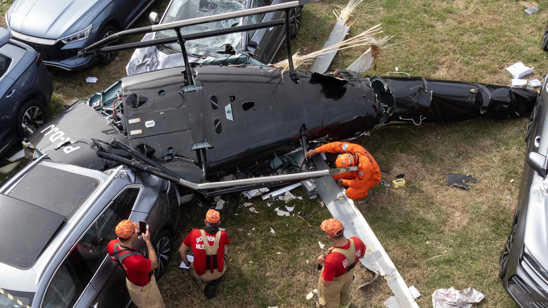 Rettungskräfte stehen bei einem auf Autos herabgestürzten Hubschrauber. | AFP