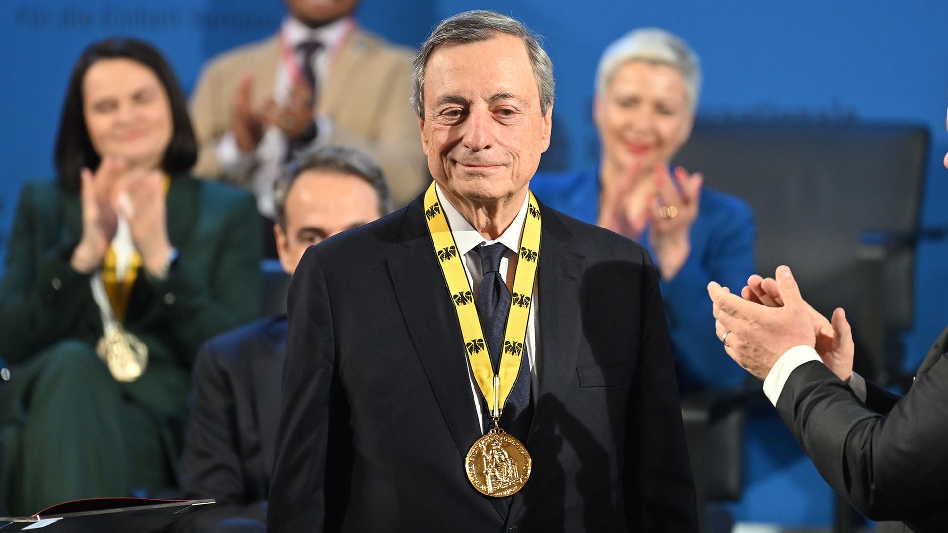 Mario Draghi steht mit dem Karlspreis im Rathaus in Aachen. | Henning Kaiser/dpa