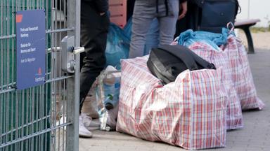 Geflüchtete warten mit gepackten Taschen vor einer Notunterkunft.
