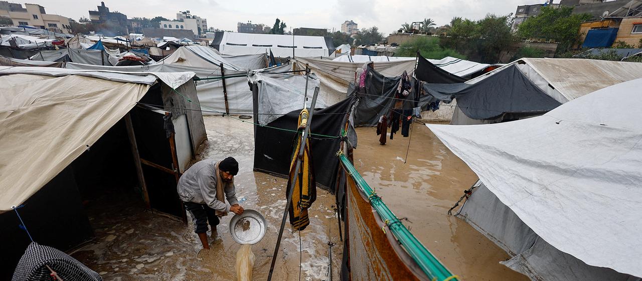Ein Mann schüttet Schlammwasser aus einem Zeltlager in Nuseirat.