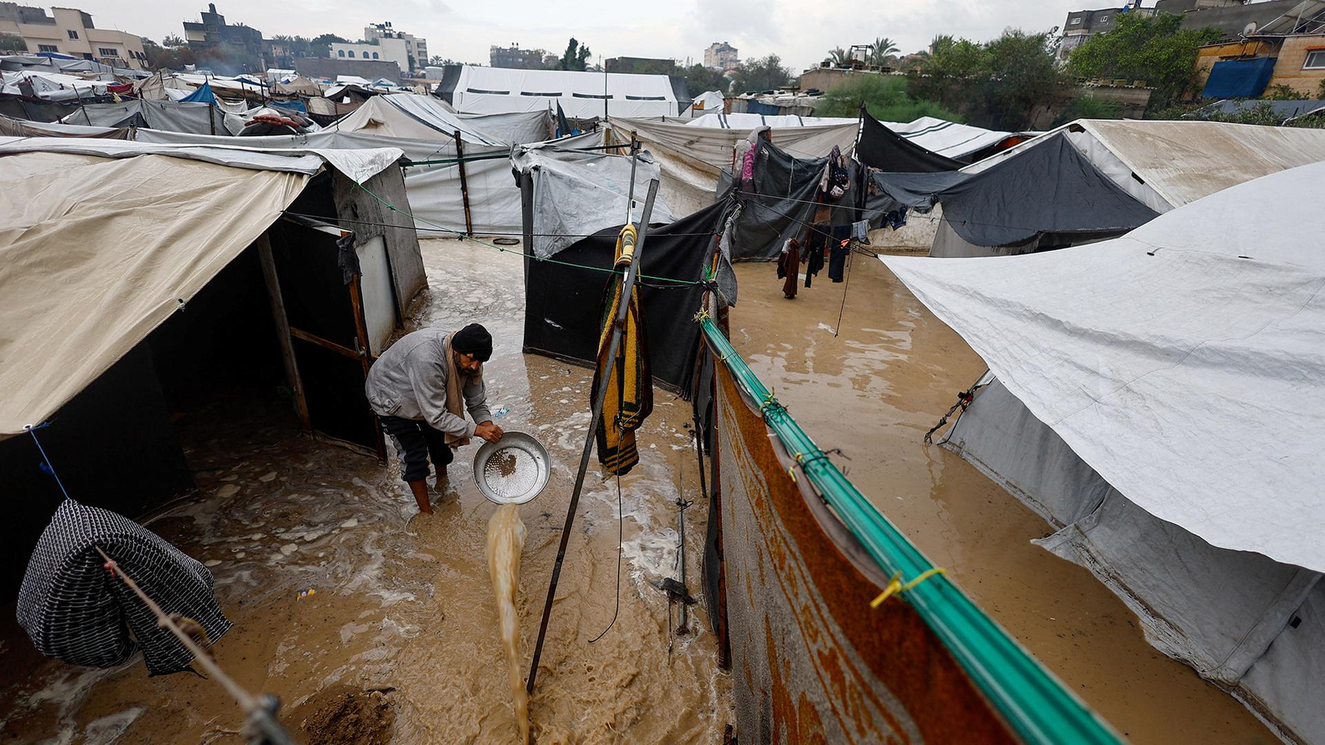 Ein Mann schüttet Schlammwasser aus einem Zeltlager in Nuseirat. | REUTERS